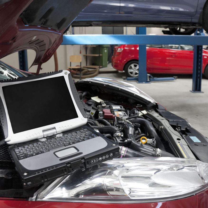 Car in a workshop and a computer running diagnostics on the engine.